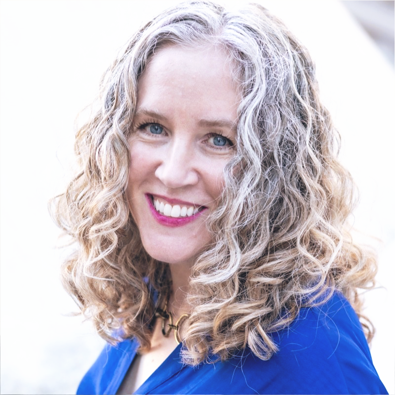 Liz Hunt — a smiling white woman with shoulder-length blond and white hair wearing a royal-blue v-neck top